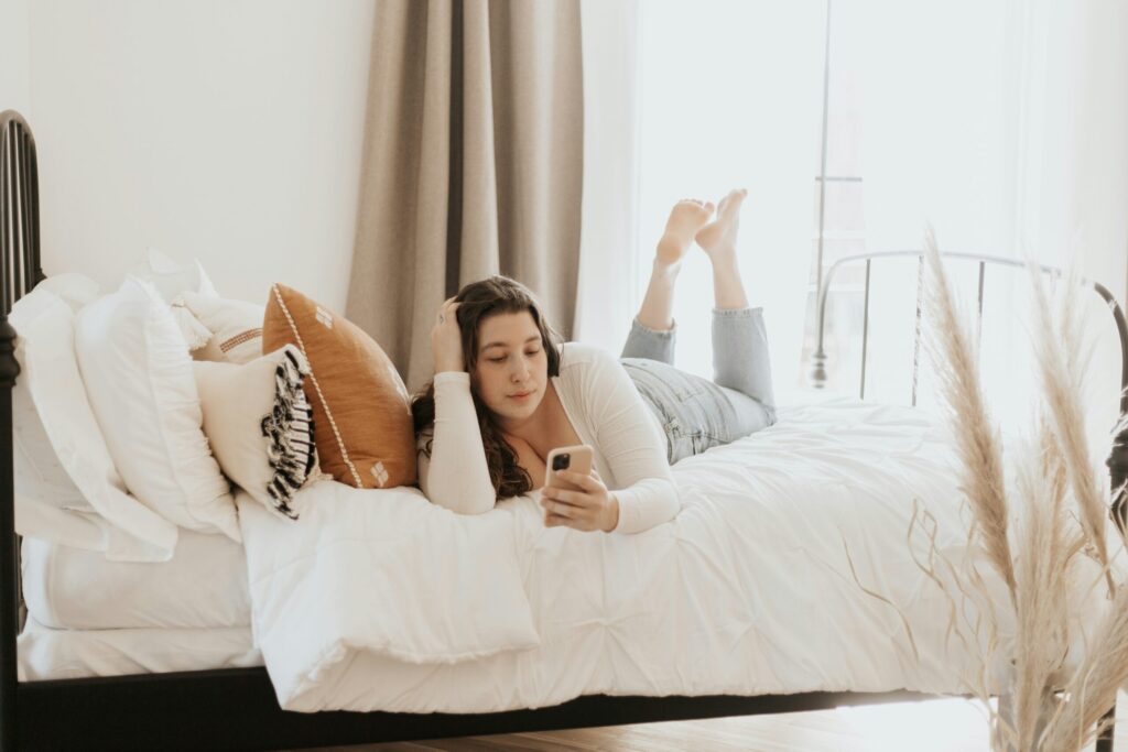 ベッドでスマホを操作する女性の写真